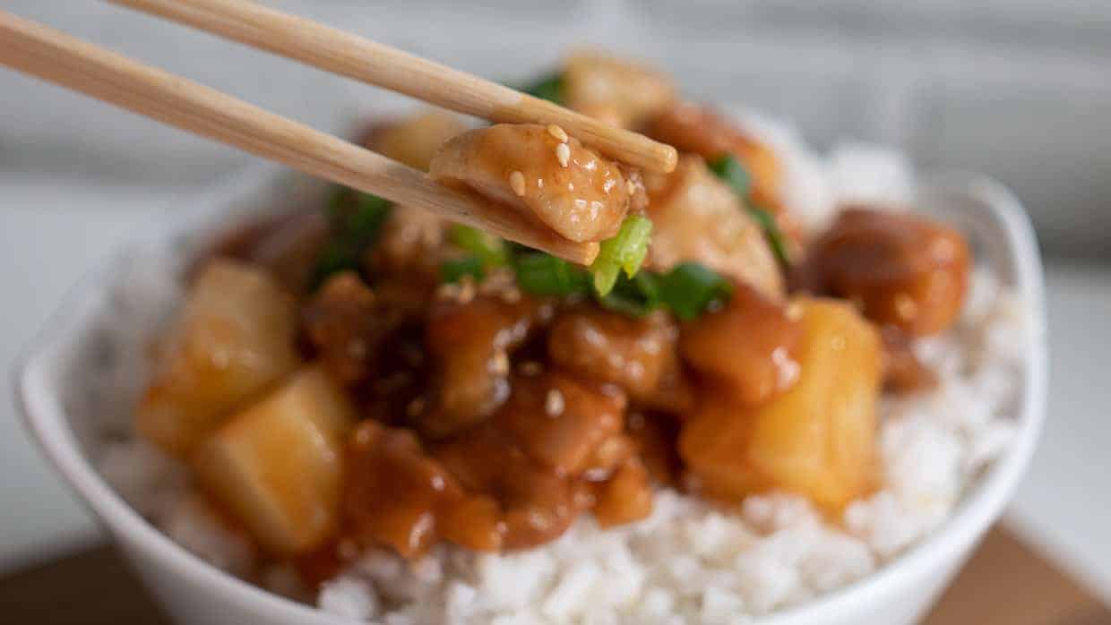 Eating sweet and sour chicken with chopsticks.