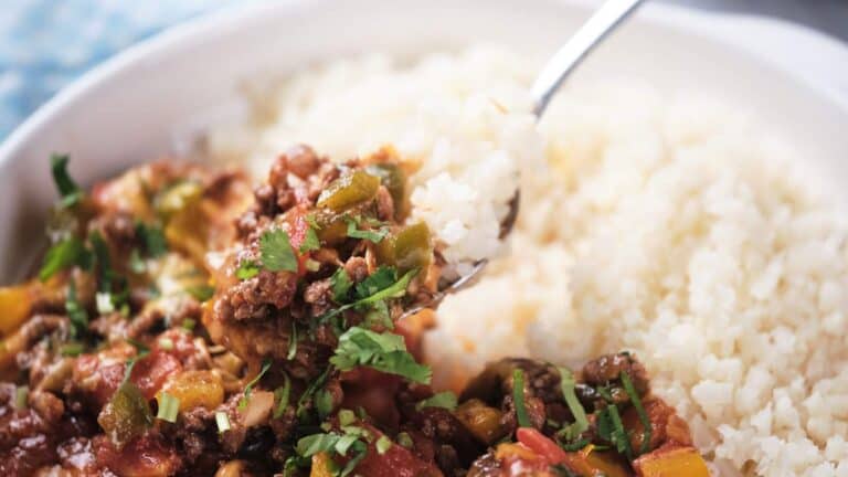 A bowl of taco skillet served with a side of cauliflower rice, garnished with fresh herbs.