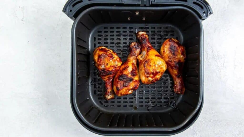 Bbq chicken legs in a black air fryer basket, showing golden-brown crispy skin.