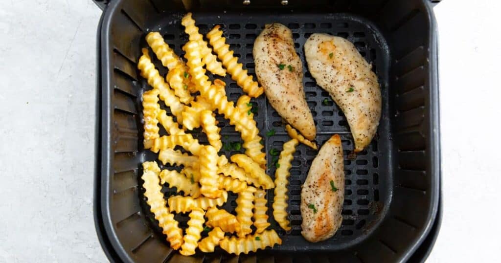 chicken tenders with fries in an air fryer basket.