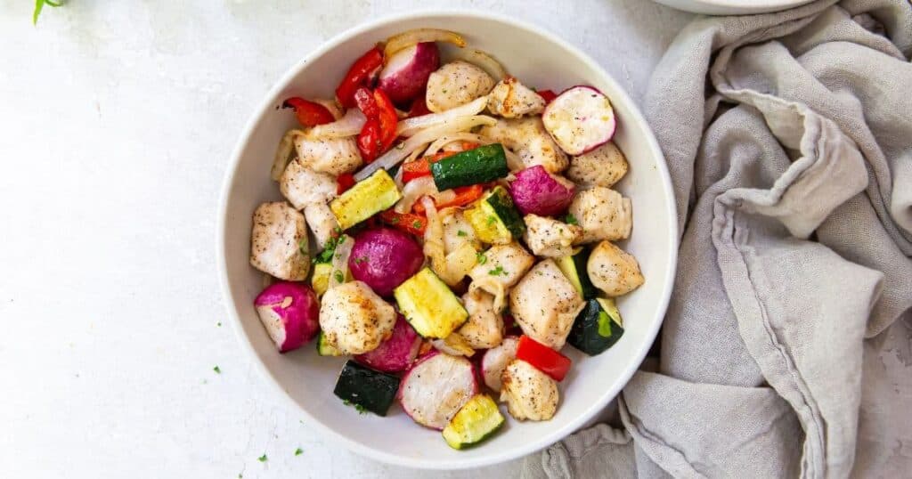 air fryer chicken and veggies in a white bowl with a grey napkin.