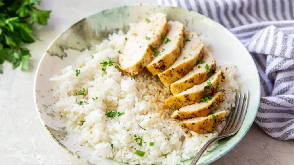 Sliced grilled chicken breast over a bed of white rice garnished with parsley in a bowl.