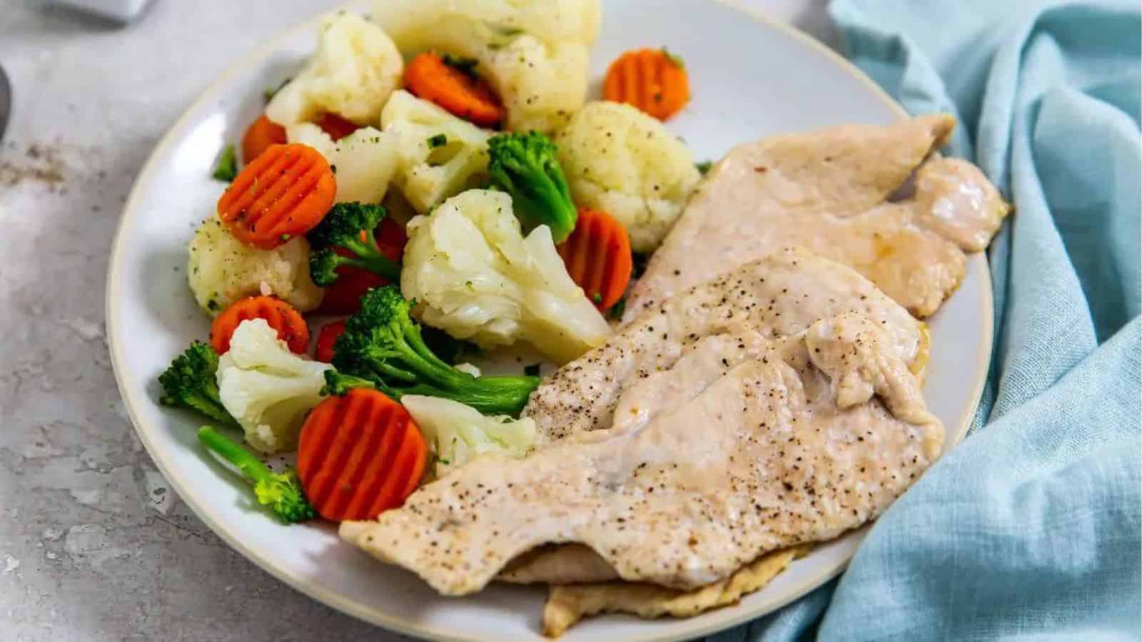 Air Fryer Thin Sliced Chicken Breast on a white plate with carrots. cauliflower, and broccoli.