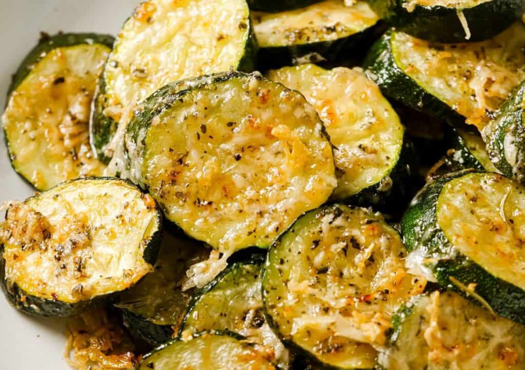 Roasted zucchini slices sprinkled with grated cheese and seasonings, close-up.