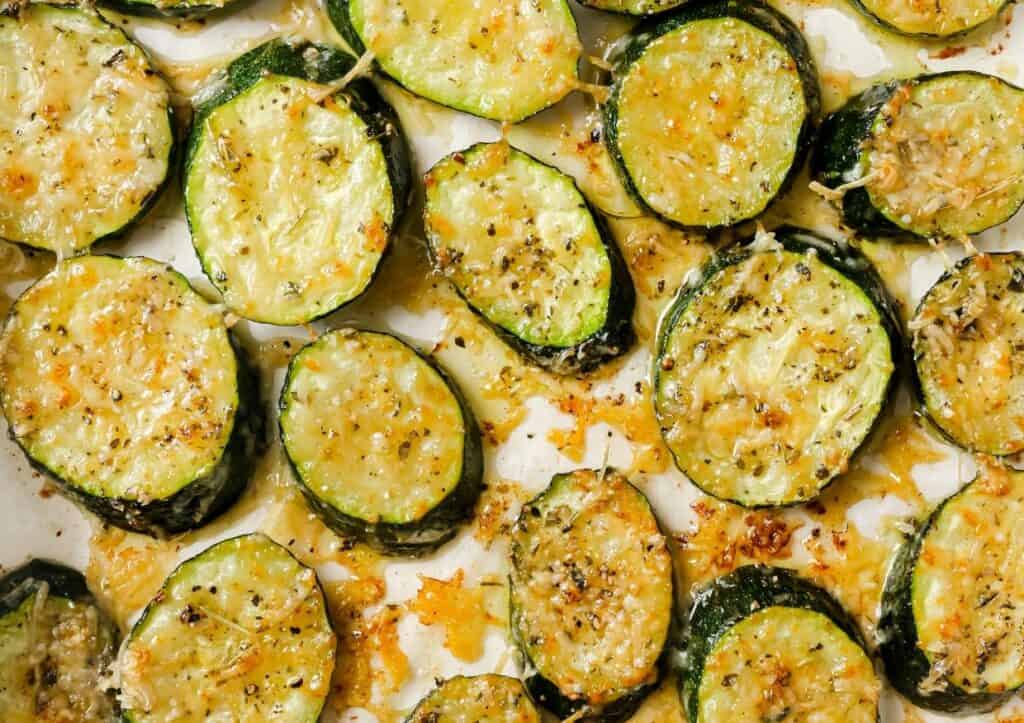 Roasted zucchini slices seasoned with herbs and parmesan cheese on a baking sheet.