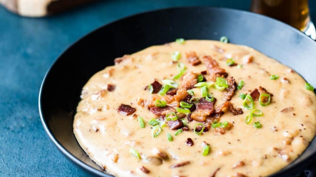 A bowl of creamy soup garnished with bacon bits and sliced green onions.