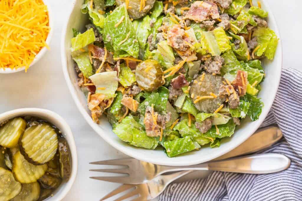 A loaded bacon cheeseburger salad with pickles on the side.