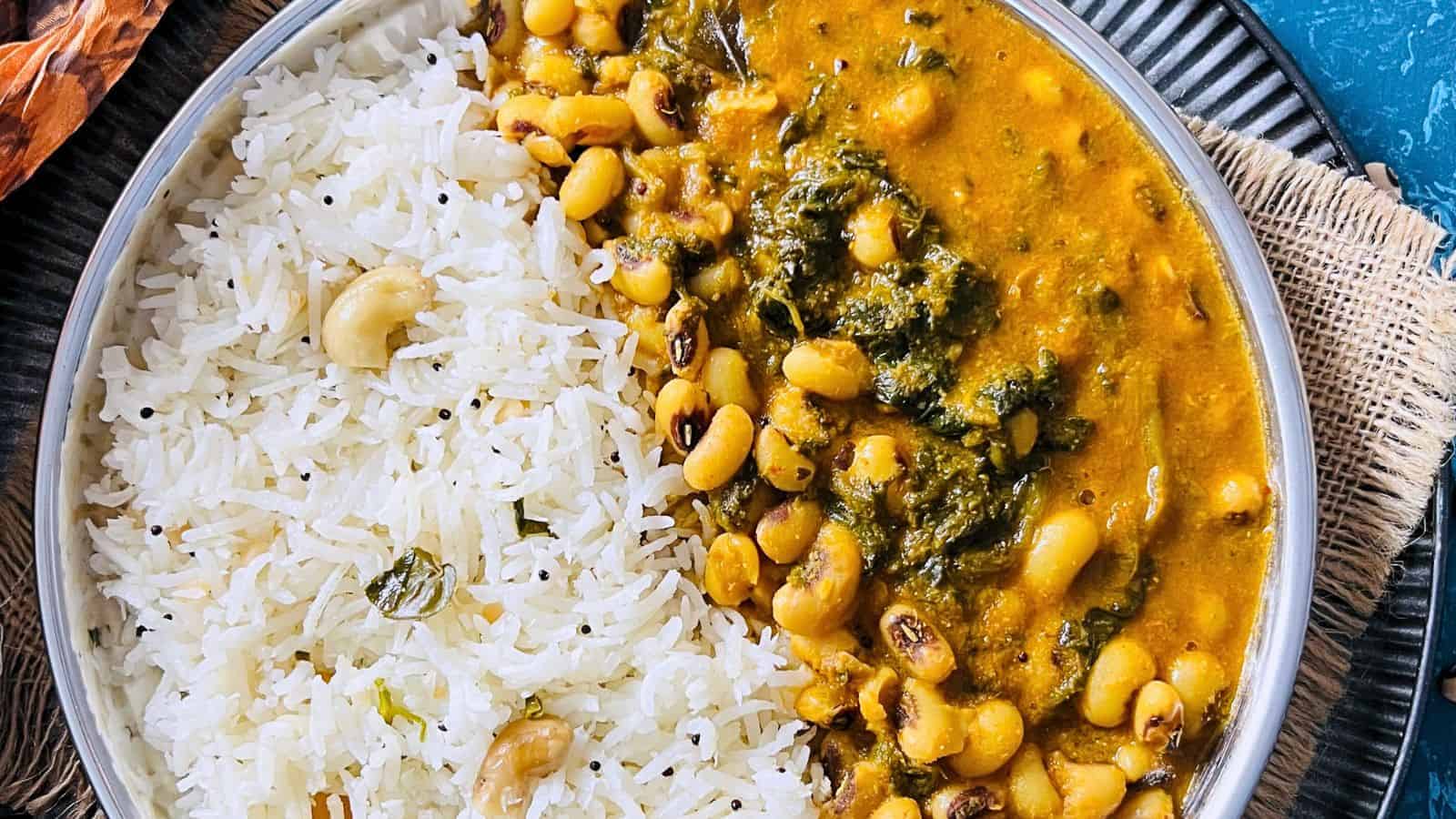 A bowl of Black-Eyed Peas Curry in Instant Pot served with white rice and cashews on a blue plate.