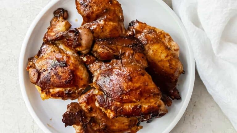 A plate of glazed roasted chicken thighs presented on a white background.