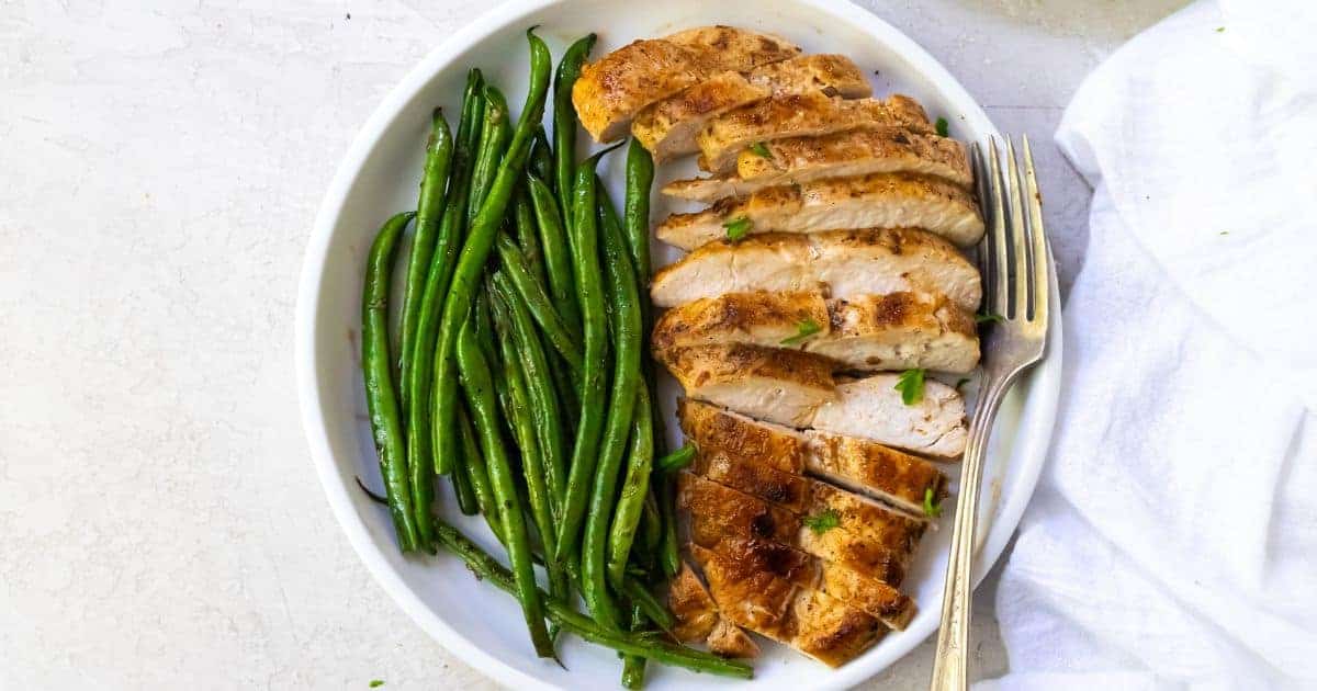 Blackstone Chicken Breast with green beans on a white plate with a fork.