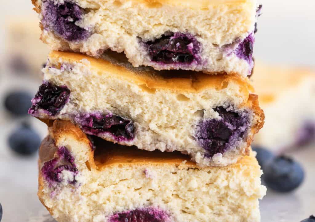 A stack of blueberry bars with layers of fresh blueberries visible in the soft, baked layers.