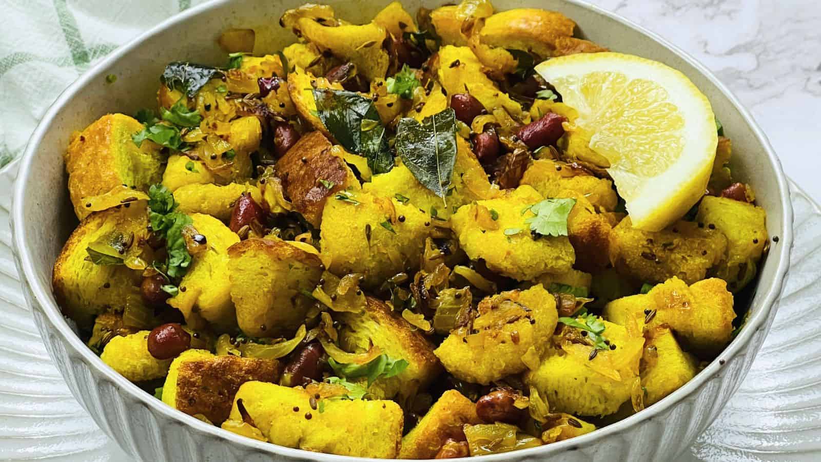 A bowl of Bread Upma with fried potatoes, spices, herbs, and lemon wedges.