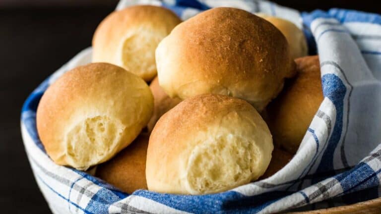 A basket of freshly baked brioche rolls covered with a blue and white checkered cloth.