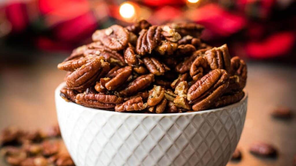 A bowl of roasted pecans with festive lights in the background.