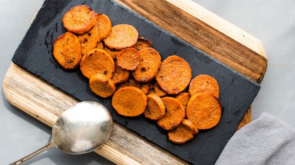 Sliced roasted sweet potatoes served on a slate board with a spoon on the side.
