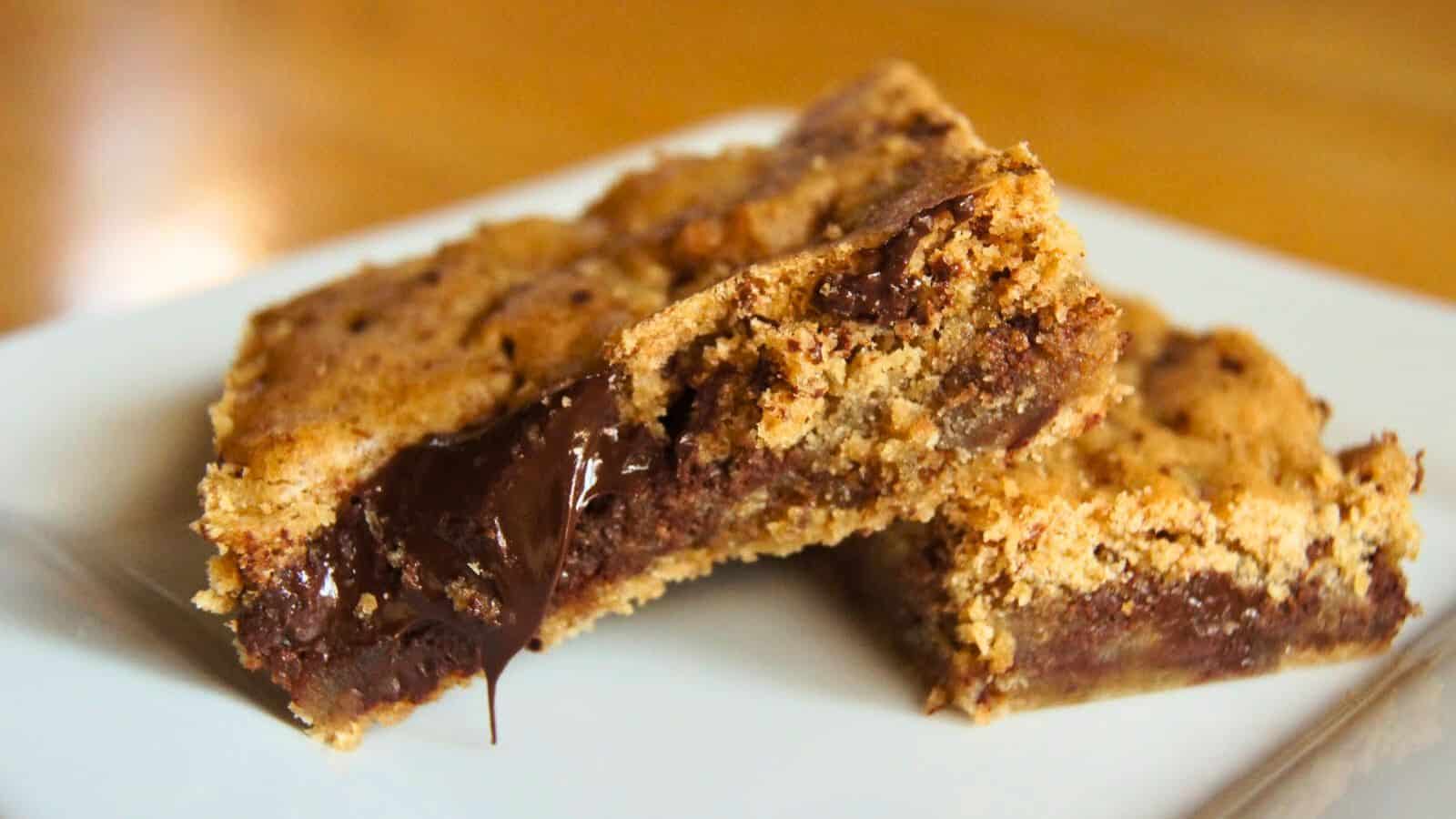 Image shows Two butterscotch brownies with melted chocolate filling on a white plate, close-up view.