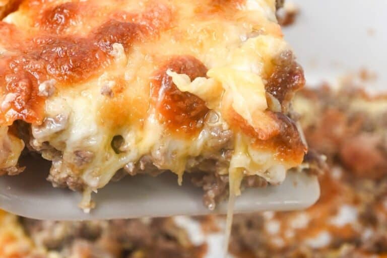 A close-up image of a slice of lasagna being lifted on a spatula, showing layers of melted cheese and meat sauce.