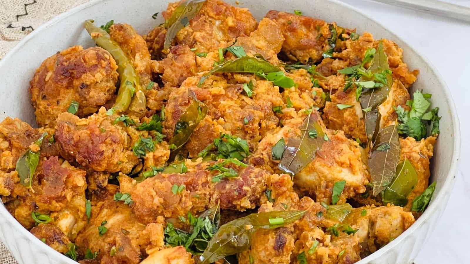 A dish of Chicken 65 seasoned with herbs and spices, garnished with chopped cilantro and green chili peppers in a white bowl.