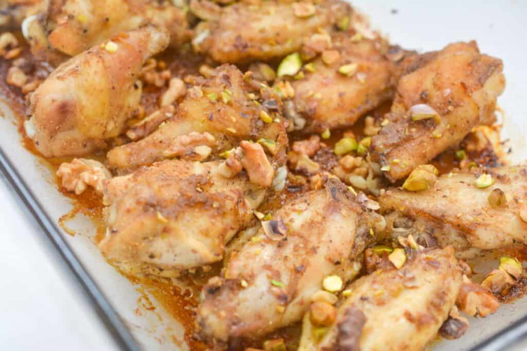 Roasted chicken wings sprinkled with crushed nuts on a baking tray.