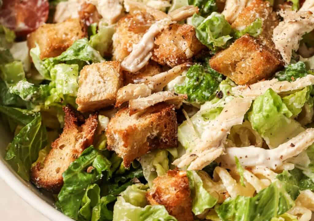 Close-up of a caesar salad with croutons, shredded chicken, and caesar dressing on chopped romaine lettuce.