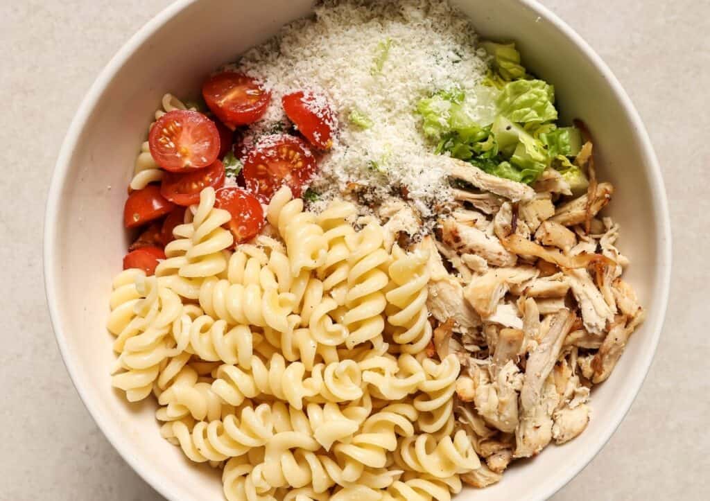 A bowl of salad with noodles, tomatoes, shredded chicken, romaine lettuce, and grated parmesan cheese.