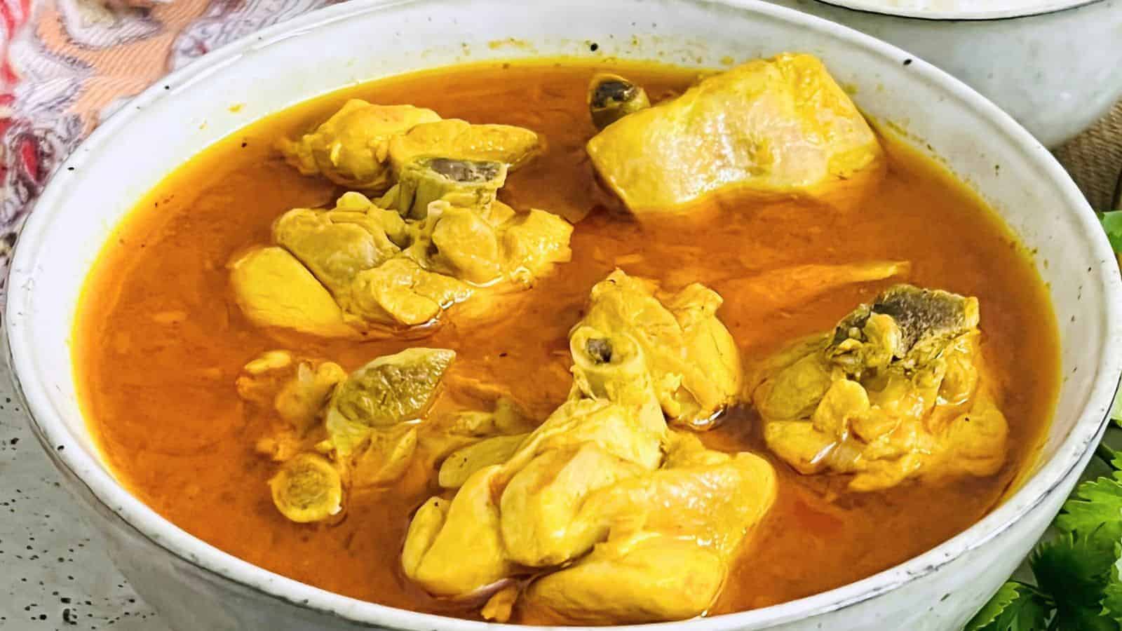 A bowl of Chicken Curry Home Style with pieces of meat and visible spices in a rich, orange sauce.