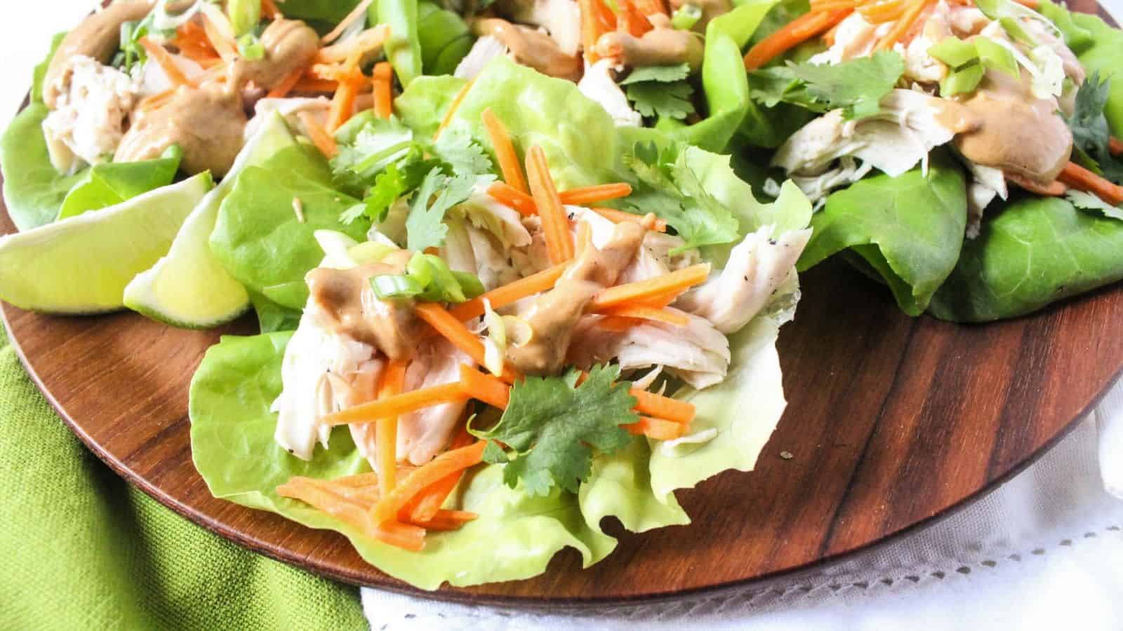 Lettuce wraps filled with shredded chicken, shredded carrots, and peanut sauce on a plate.