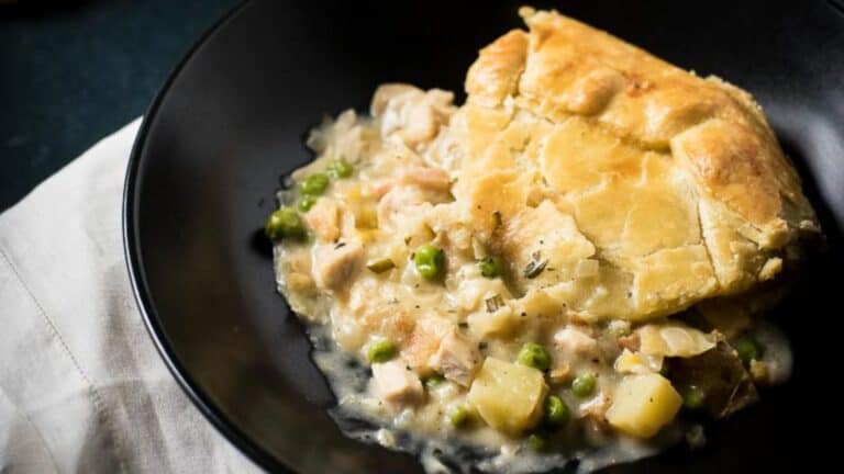 A serving of chicken pot pie on a black plate, featuring a golden-brown crust and visible filling with chicken, peas, and potatoes.