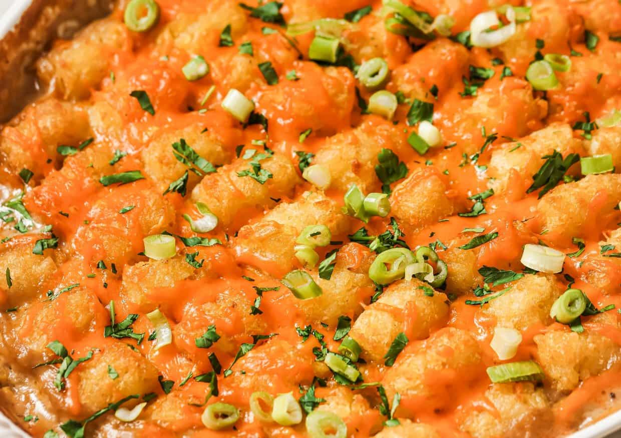 A casserole dish filled with tater tots, shredded chicken, and corn, topped with melted cheese and green onions.