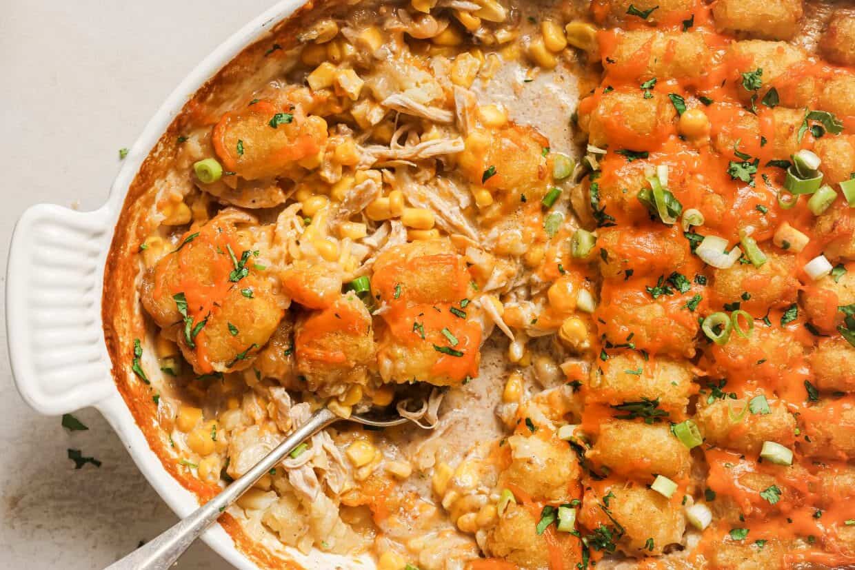 A casserole dish filled with tater tots, shredded chicken, and corn, topped with melted cheese and green onions.