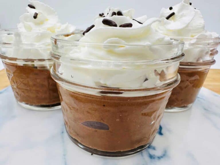 Three glass jars filled with chocolate mousse topped with whipped cream and chocolate chips on a marbled surface.