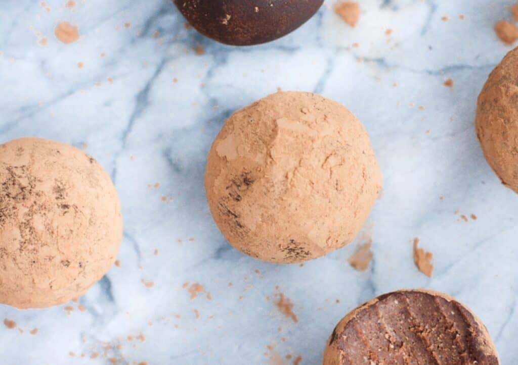 An assortment of chocolate truffles dusted with cocoa powder viewed from above on a marble surface.