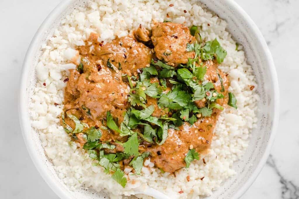 A bowl of rice topped with meatballs in a creamy sauce, garnished with fresh cilantro.