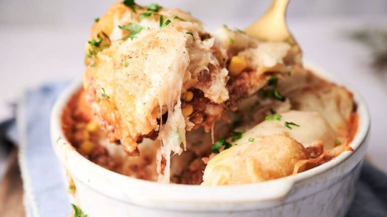 A close-up of a cowboy casserole in a ceramic dish, topped with melted cheese and garnished with fresh herbs.