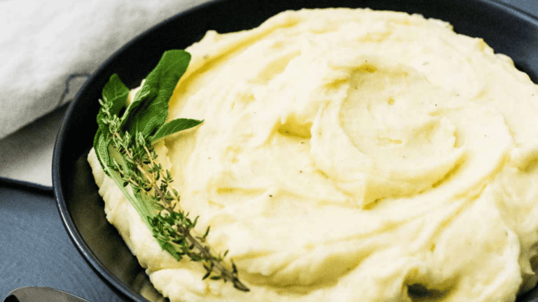 Creamy mashed potatoes garnished with fresh herbs in a black dish.