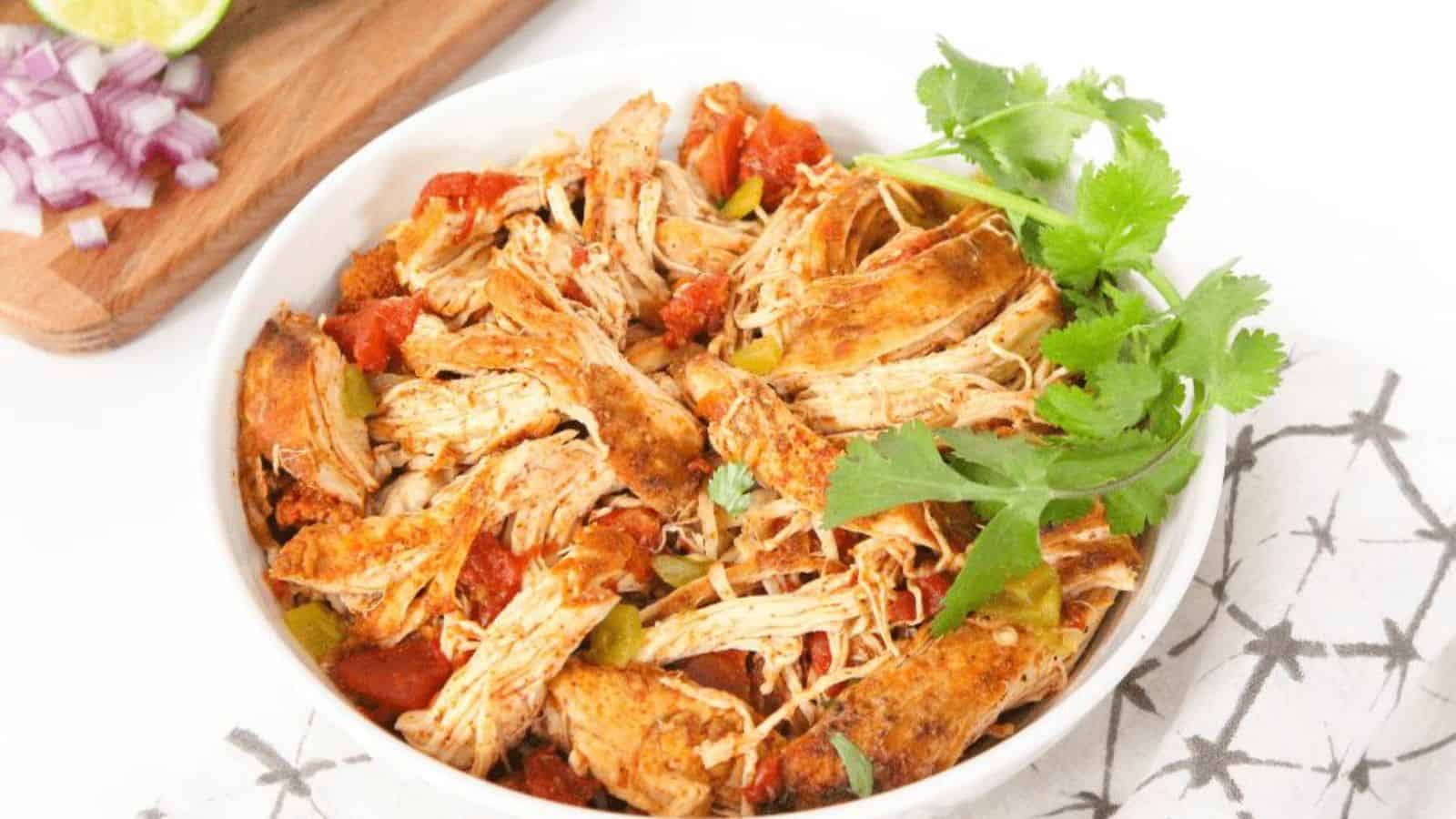 A white bowl with shredded chicken, diced tomatoes, and green chilis.