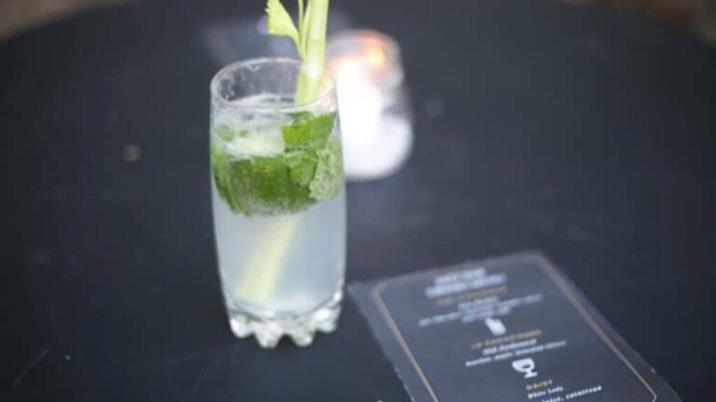 A refreshing mojito with a sprig of mint, served on a dark table next to a menu.