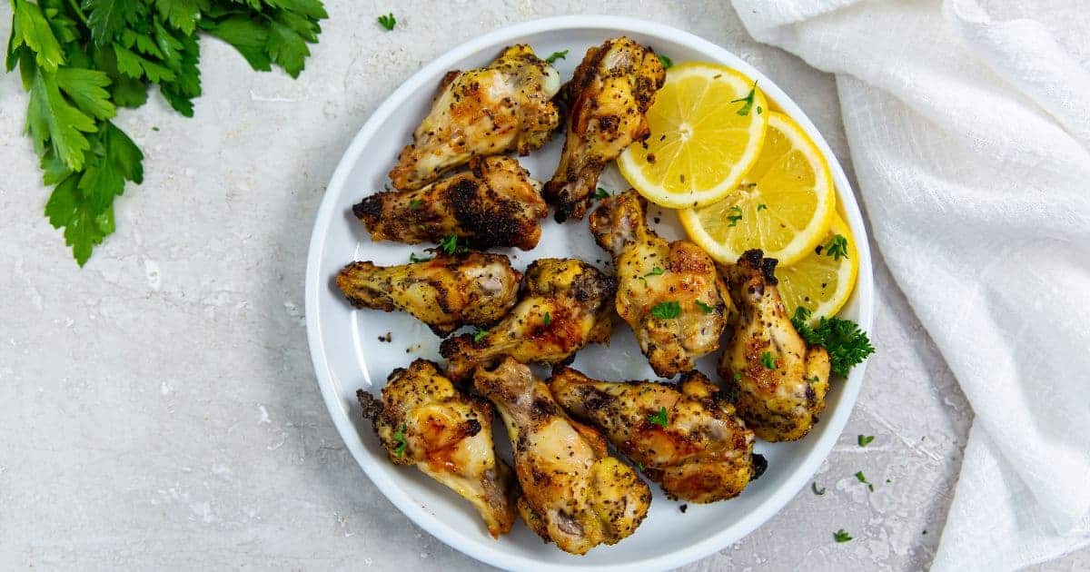 Delicious Air Fryer Lemon Pepper Chicken Wings on a white plate with lemon and parsley.
