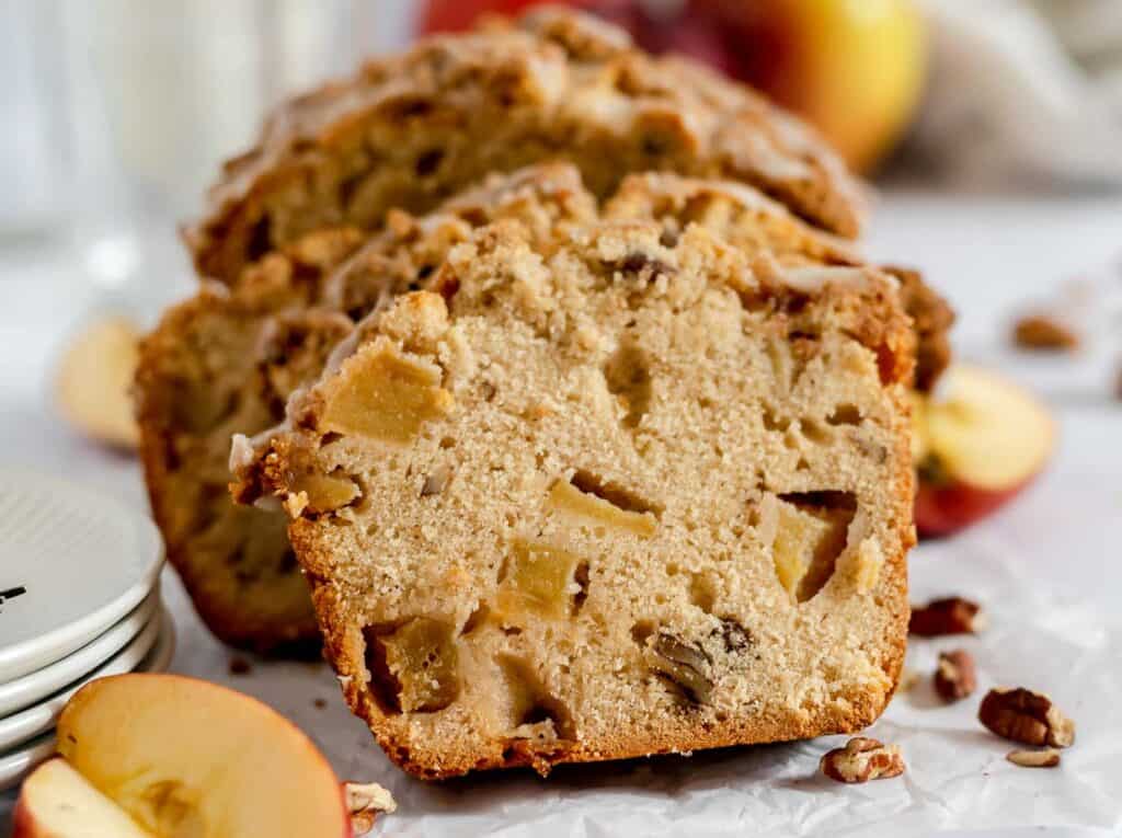 Sliced apple walnut bread on a white plate, with fresh apples and walnuts around, on a light background.