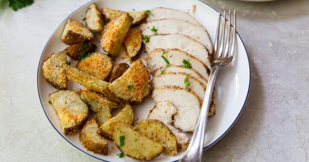 sliced air fryer chicken breasts and potatoes with a fork on a white plate