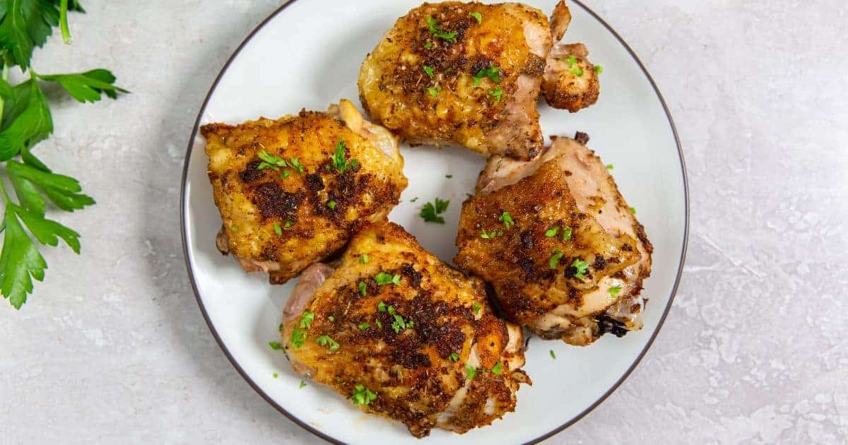 Easy Air Fryer Keto Chicken Thighs on a white plate with parsley and a fork.