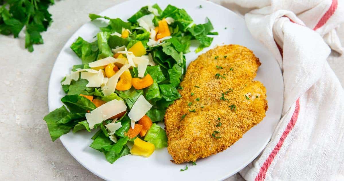 Easy Air Fryer Shake n Bake Chicken Breast on a white plate with a salad topped with bell peppers and parmesan.