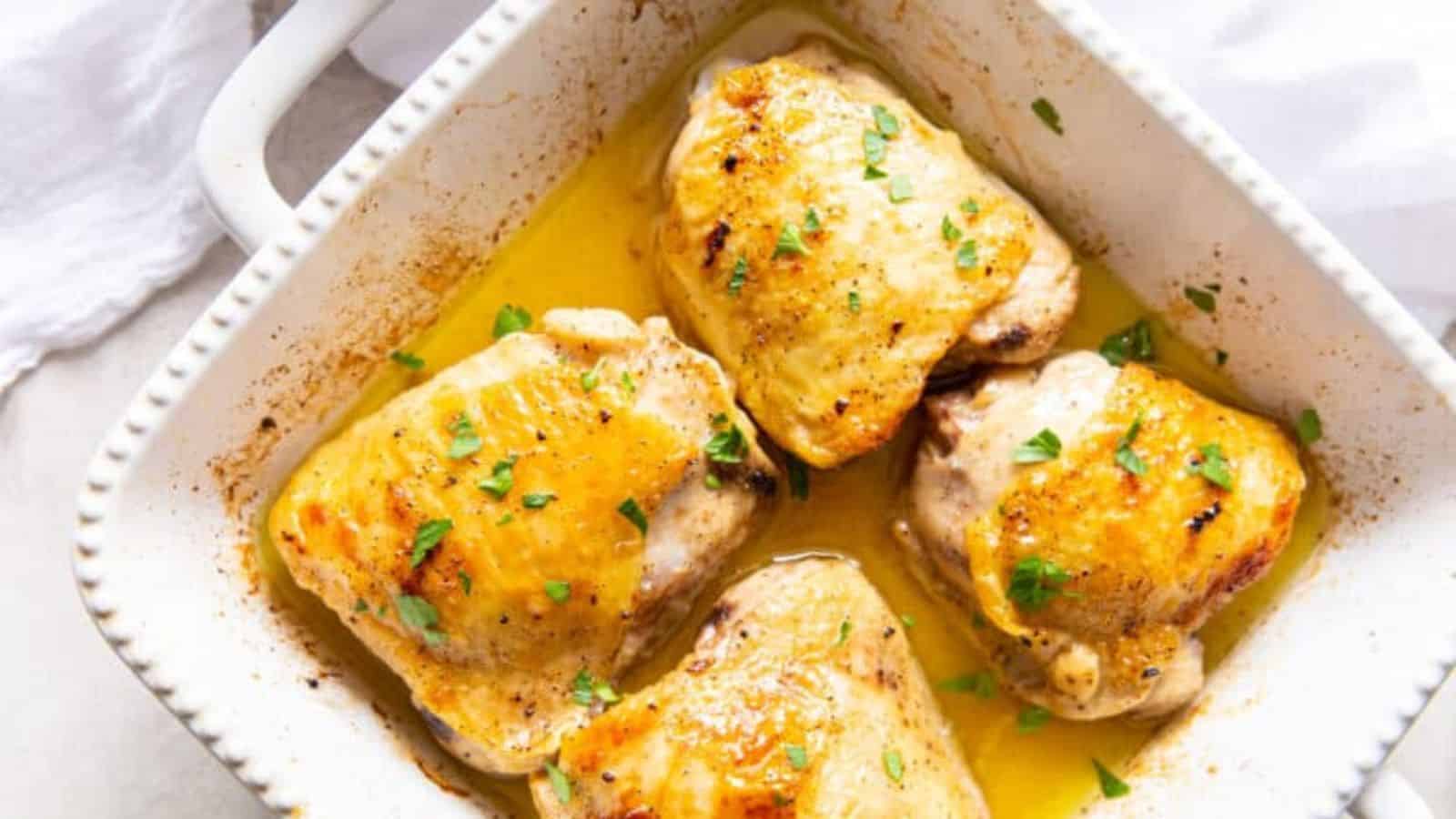 Easy Garlic Broiled Chicken Thighs with parsley in a white baking dish with a spatula.