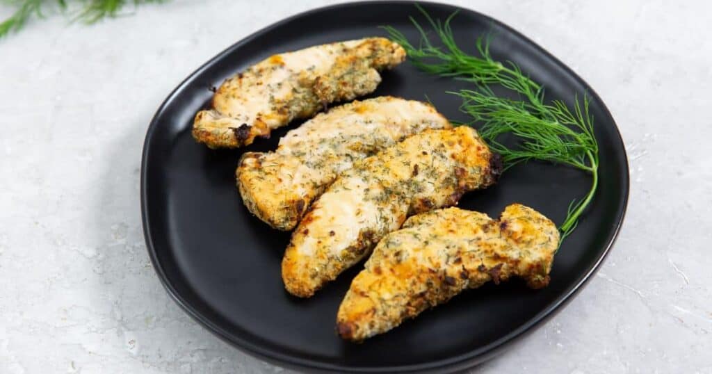 Easy air fryer ranch chicken tenders on a black plate with fresh dill garnish on a light marble surface.