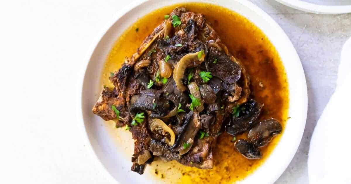 Easy Keto Crockpot Pork Chops with mushrooms, onions and parsley on a white plate.