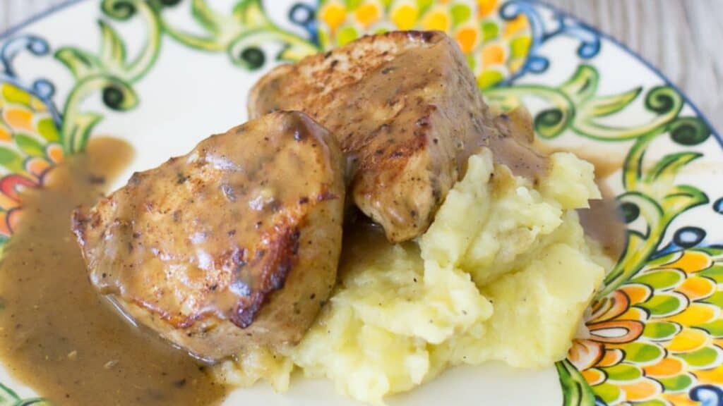 Grilled pork chops with gravy served alongside mashed potatoes.