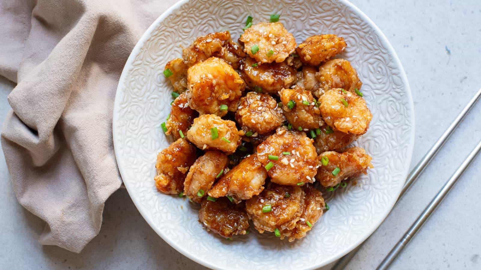 Fried shrimp with sauce and sesame seeds and chives in white bowl.