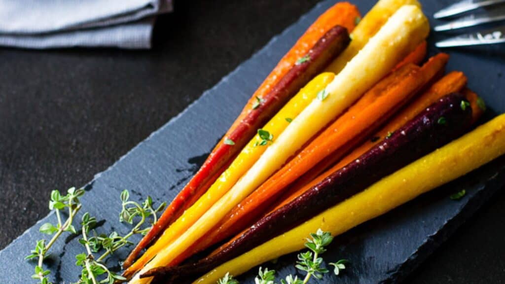 Roasted multicolored carrots arranged on a slate serving platter, garnished with fresh herbs.