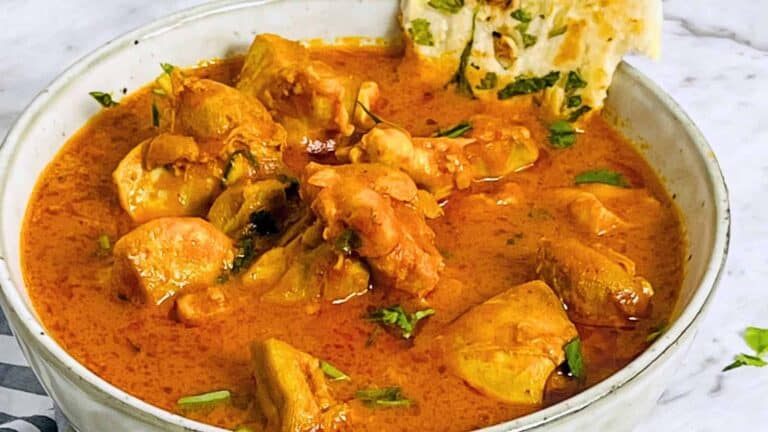 A bowl of Instant Pot Butter Chicken garnished with cilantro, accompanied by naan bread on a white marble surface.