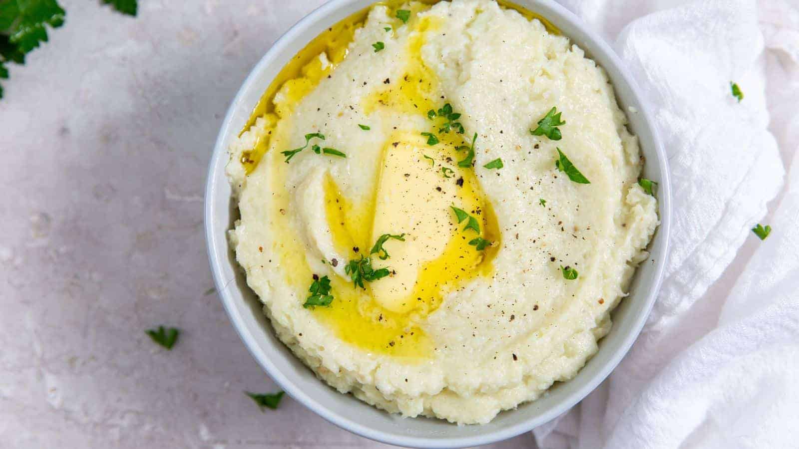 Instant Pot Cheesy Mashed Cauliflower in a white bowl with butter, salt, pepper, and parsley.